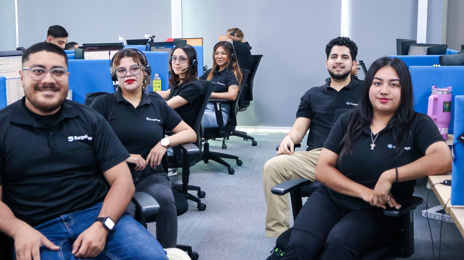 SurgePays operations center team members at their desks, smiling at the camera